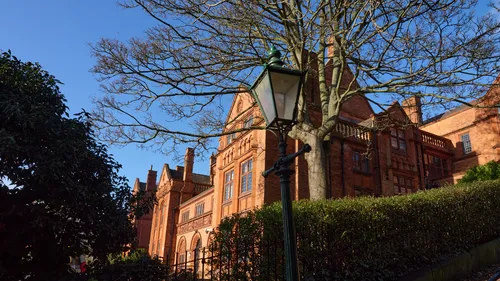 Lincoln technical college winter lamppost This image captures a bright winter afternoon at Lincoln Technical College in Lincoln, England, United Kingdom. The architectural photograph prominently features the historic red-brick façade of the college, with its intricate Victorian design highlighted by the clear, blue sky and the crisp winter sunlight. In the foreground, an old-fashioned lamppost stands beneath a leafless tree, typical of the winter season, while the well-maintained hedges and bare branches accentuate the serene atmosphere. The landmark college building, with its tall chimneys and stonework details, serves as the main subject, reflecting the rich educational heritage found in Lincoln, England.